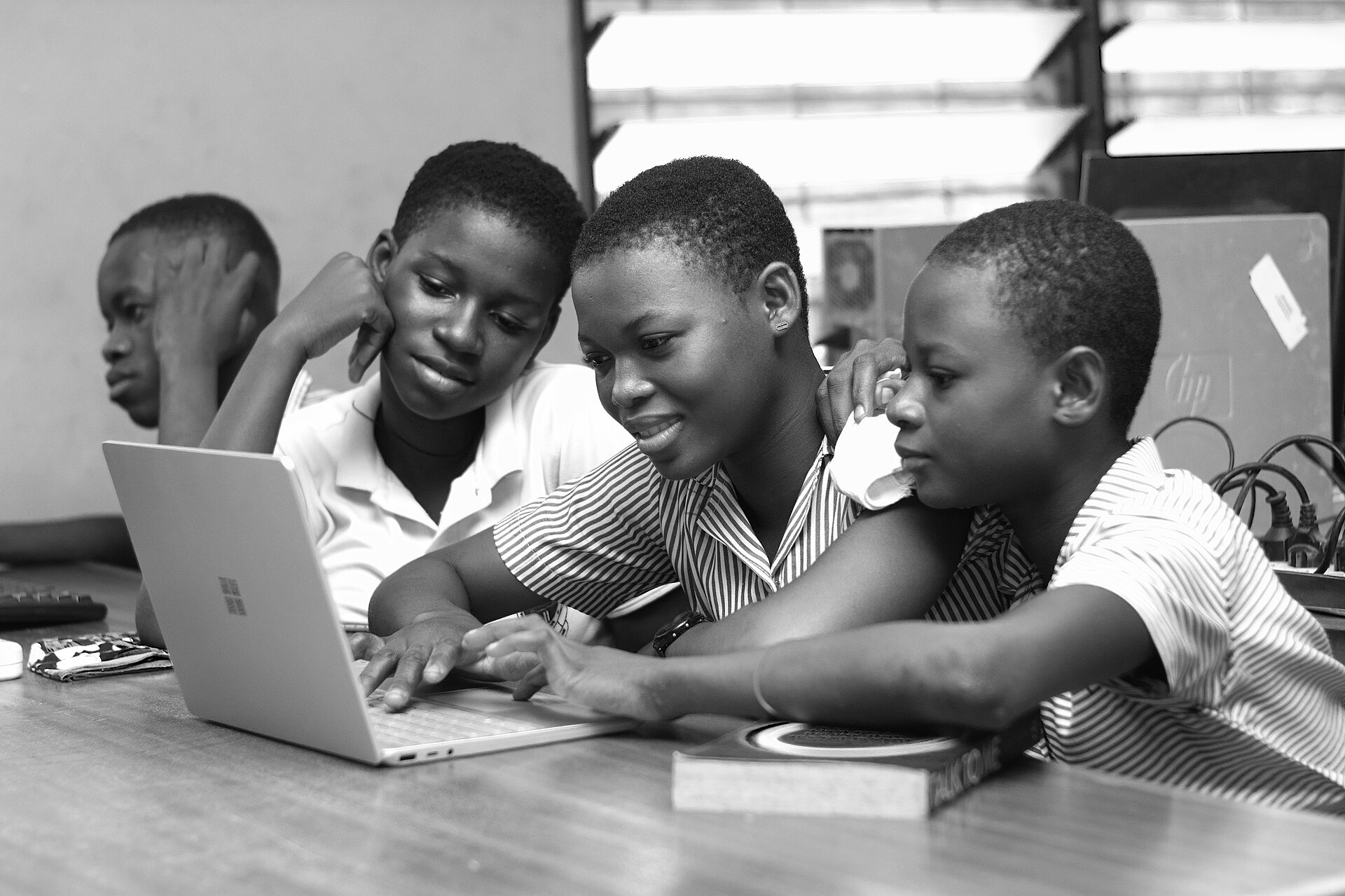Three students sharing one laptop and smiling as they work together