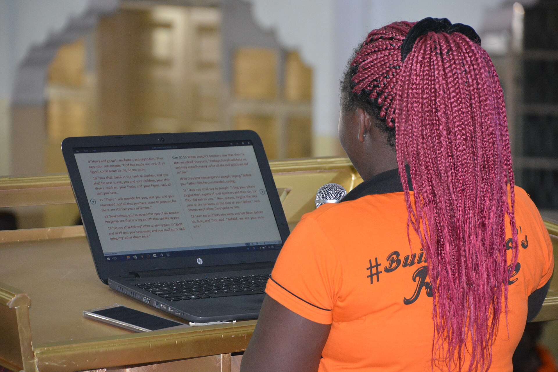 A student in an orange shirt working on a laptop at a lectern